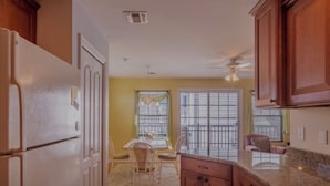 A kitchen with wooden cabinets, a granite countertop, and a dining area with a table and chairs.