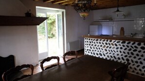 Et spiseområde med et træbord og stole, et køkken med et hvidt flisebaggrund og en hængende lampe.