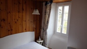 Et soveværelse med træloft, en enkelt seng, et lille natbord, et vindue med gardiner og en hængende lampe.