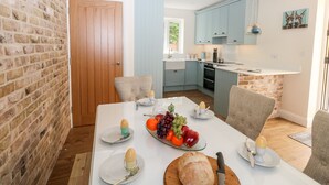 A dining area with a brick wall, a wooden door, and a kitchen in the background. - The Chocolate Box (Weymouth)