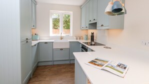 A modern kitchen with light blue cabinets, a white countertop, and a window providing natural light. - The Chocolate Box (Weymouth)