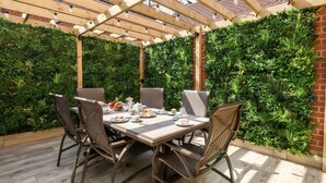 An outdoor patio with a wooden pergola, a table set for dining, and a lush green vertical garden wall. - The Chocolate Box (Weymouth)