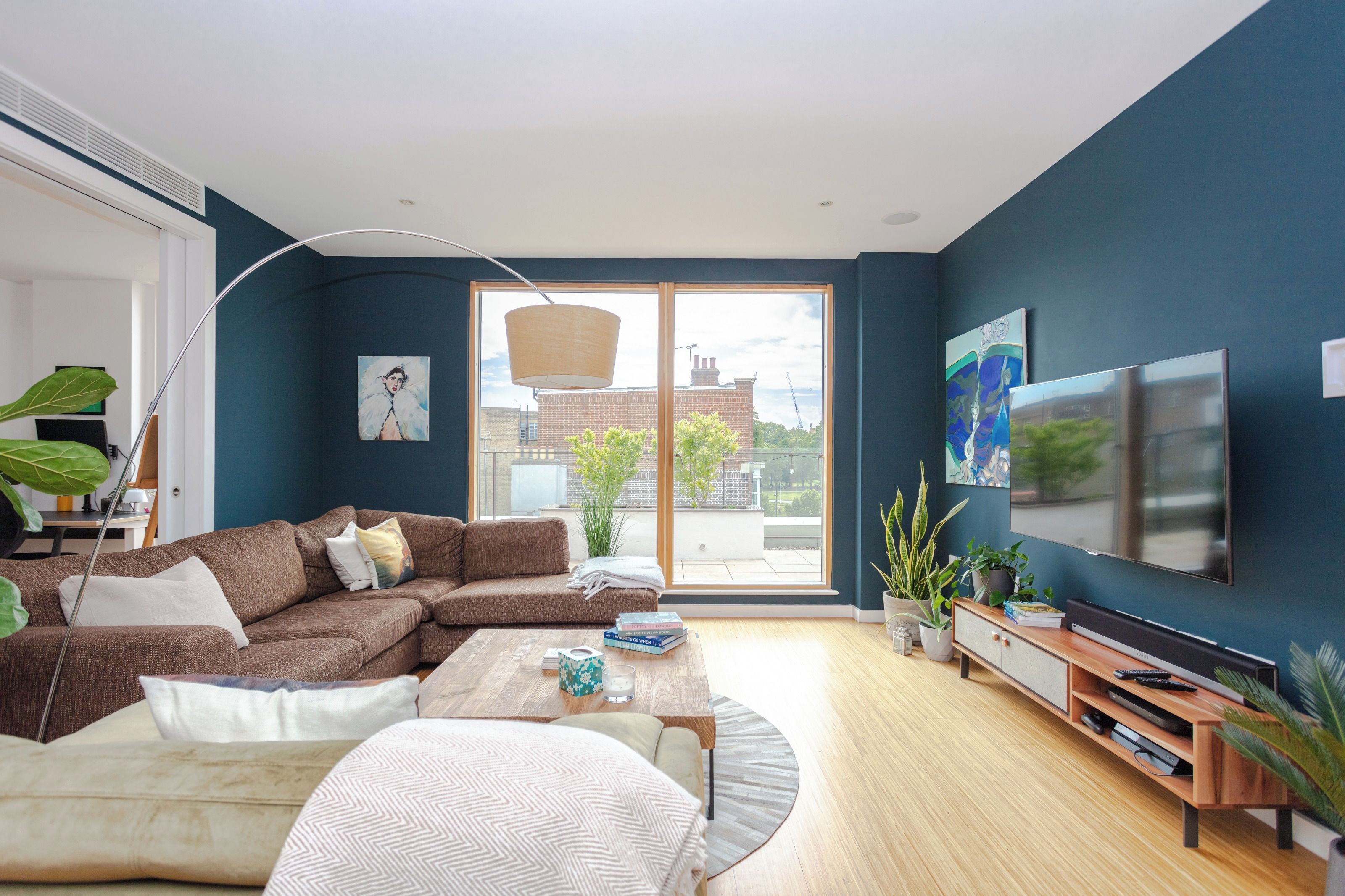 A modern living room with a sectional sofa, a coffee table, a TV, and a large window offering a view of the city.
