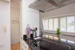 A modern kitchen with a black countertop, stainless steel appliances, and a window with blinds. - Stylish 1BD by Northcote Road and Clapham Junction (London)