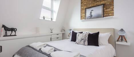 A bedroom with a bed, a nightstand, a lamp, a window, and a brick wall.