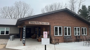 A wooden building with a 'Welcome' sign, a 'No Parking' sign, and a sign requesting dogs to be kept on a leash or in a kennel. - Rustic hunt club lodge in the heart of Minnesota lakes country... (Ashby)