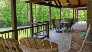 Une terrasse extérieure couverte, dotée de chaises et de tables en bois, et entourée d’arbres.