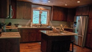 Une cuisine avec des meubles en bois, un réfrigérateur en acier inoxydable et une fenêtre donnant sur un paysage verdoyant.