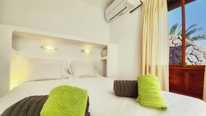 A hotel room with a bed, pillows, an air conditioning unit, and a view of palm trees. - Villa Magica 7 min walking to center, pool & A/C (Playa Blanca)