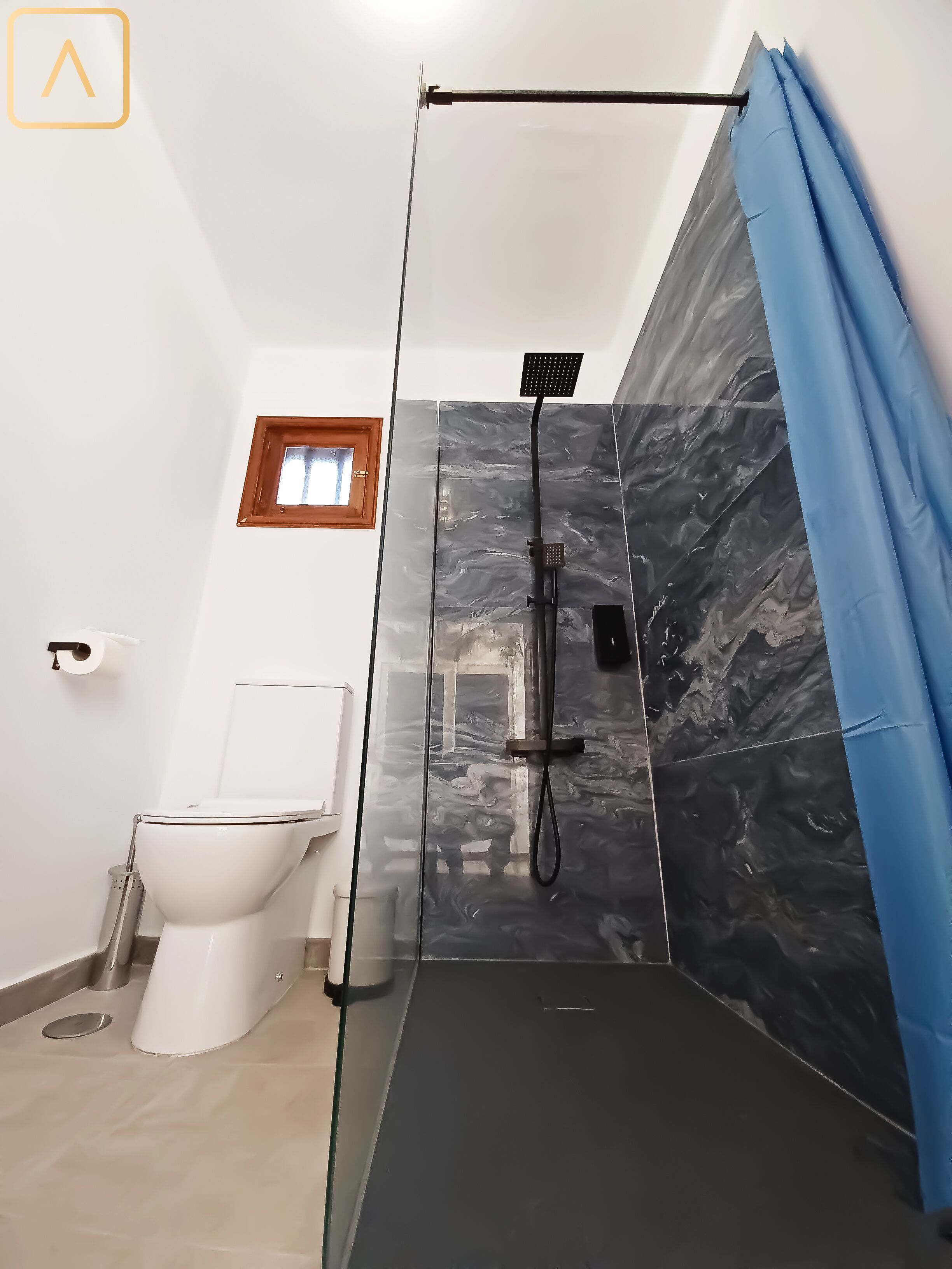Baño con ducha, inodoro y una ventana pequeña.