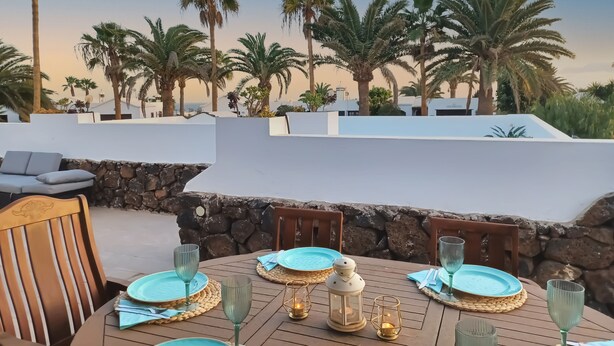 A dining table set with plates, glasses, and a lantern, overlooking palm trees and a clear sky. - Villa Magica 7 min walking to center, pool & A/C (Playa Blanca)