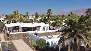 A white villa with a stone wall, palm trees, and mountains in the background. - Villa Magica 7 min walking to center, pool & A/C (Playa Blanca)