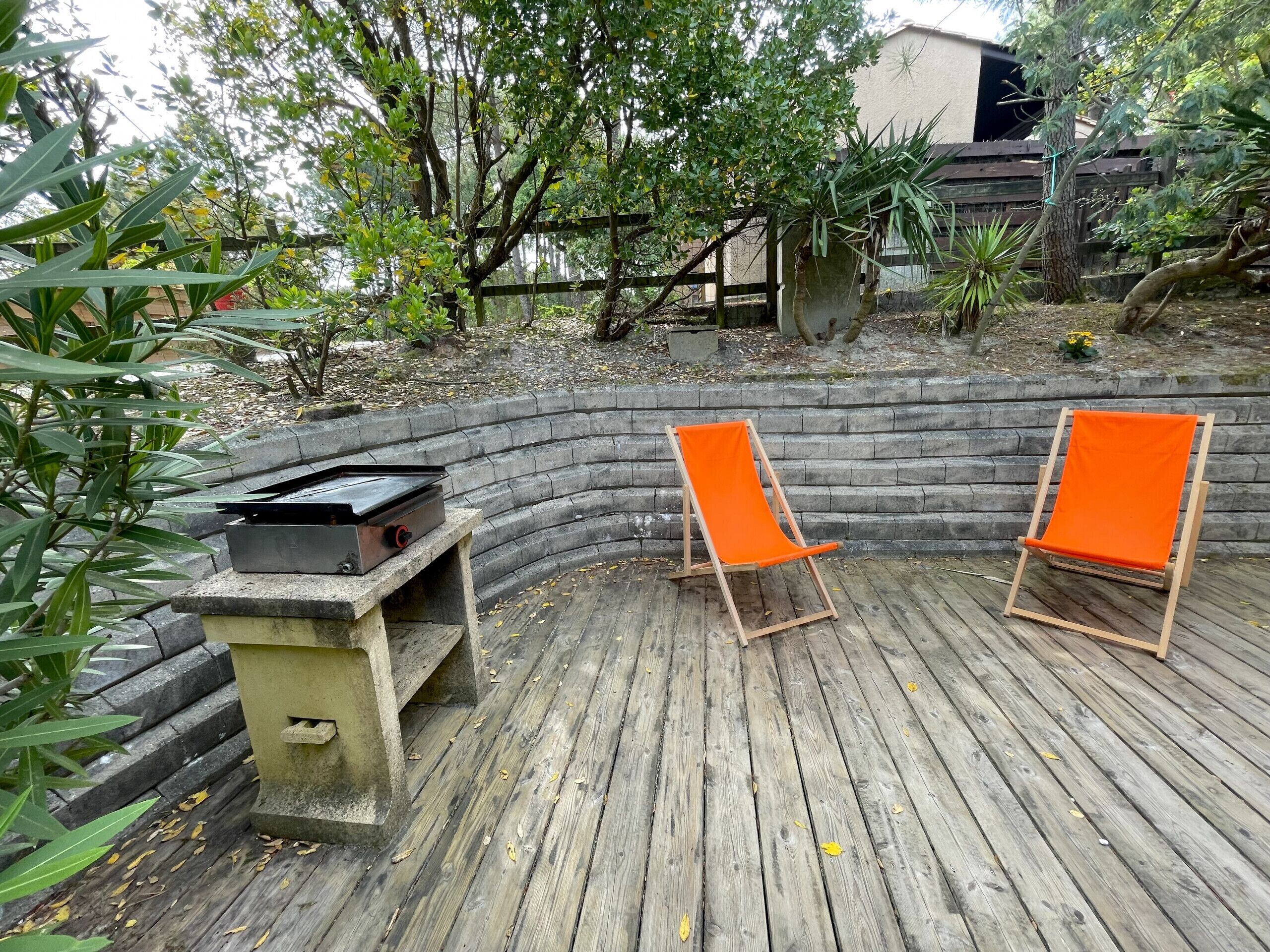A wooden deck with two orange chairs and a barbecue grill.