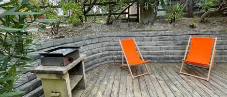A wooden deck with two orange chairs and a barbecue grill.