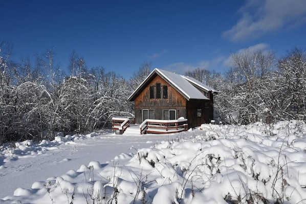 A wooden cabin with a porch, surrounded by snow-covered trees.