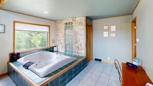 Une salle de bain spacieuse avec une grande baignoire, un mur en pierre et une fenêtre avec des stores.