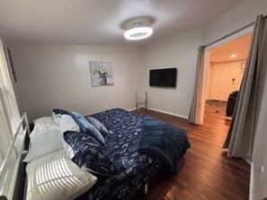 A bedroom with a bed, a painting, a television, and a door leading to another room.