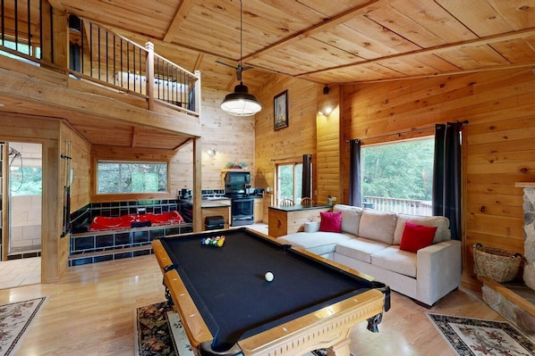 L’intérieur d’un chalet en bois comprend une table de billard, un canapé, une cuisine et un balcon.