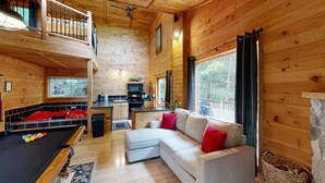 A wooden cabin interior with a pool table, a sofa, a kitchen, and a balcony. - The Hideaway (Norwalk)