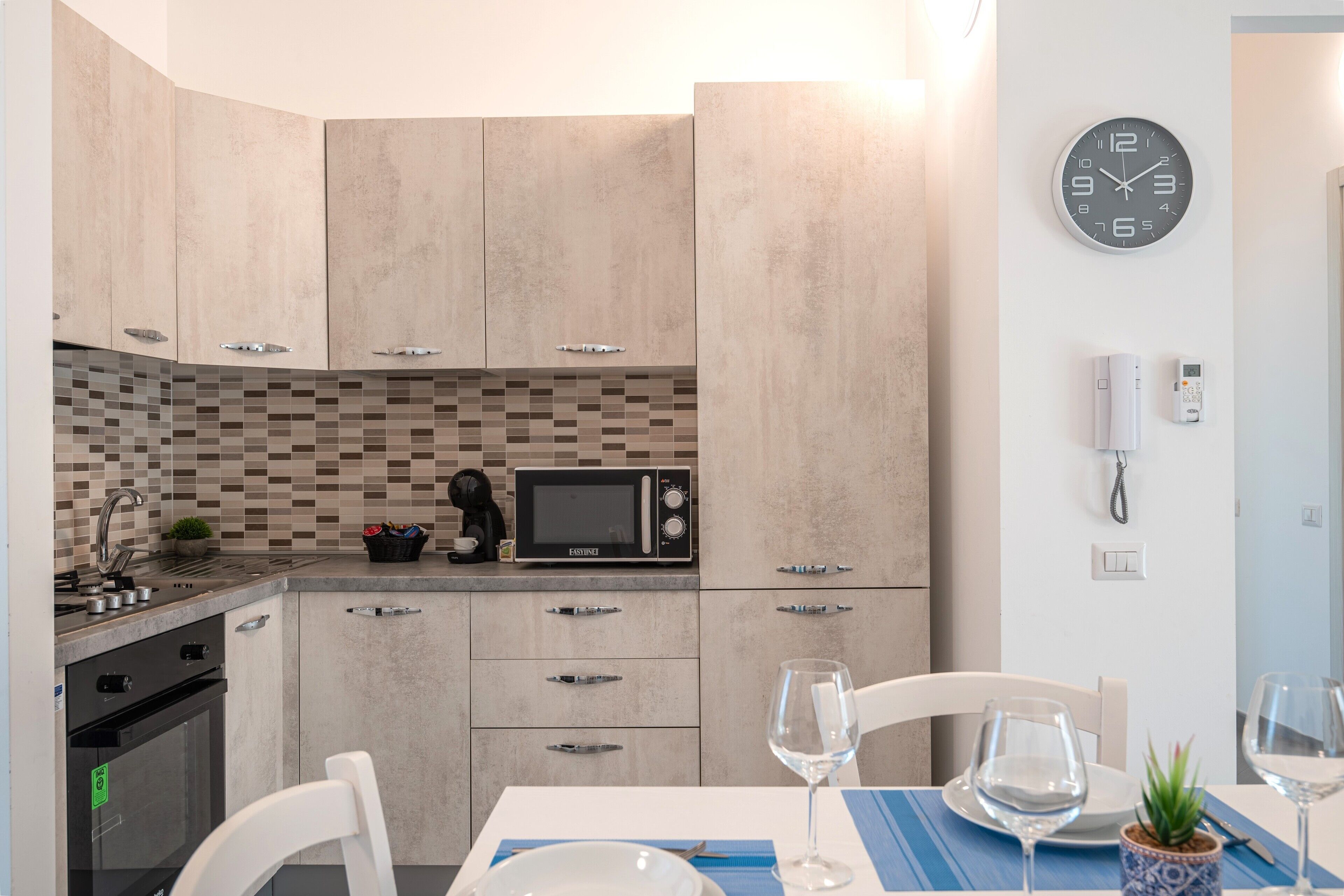 Una cocina moderna con microondas, estufa y armarios. Hay una mesa de comedor con sillas y copas de vino.