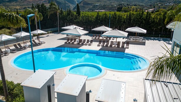 Una piscina con sillas de descanso y sombrillas, rodeada de montañas y vegetación.