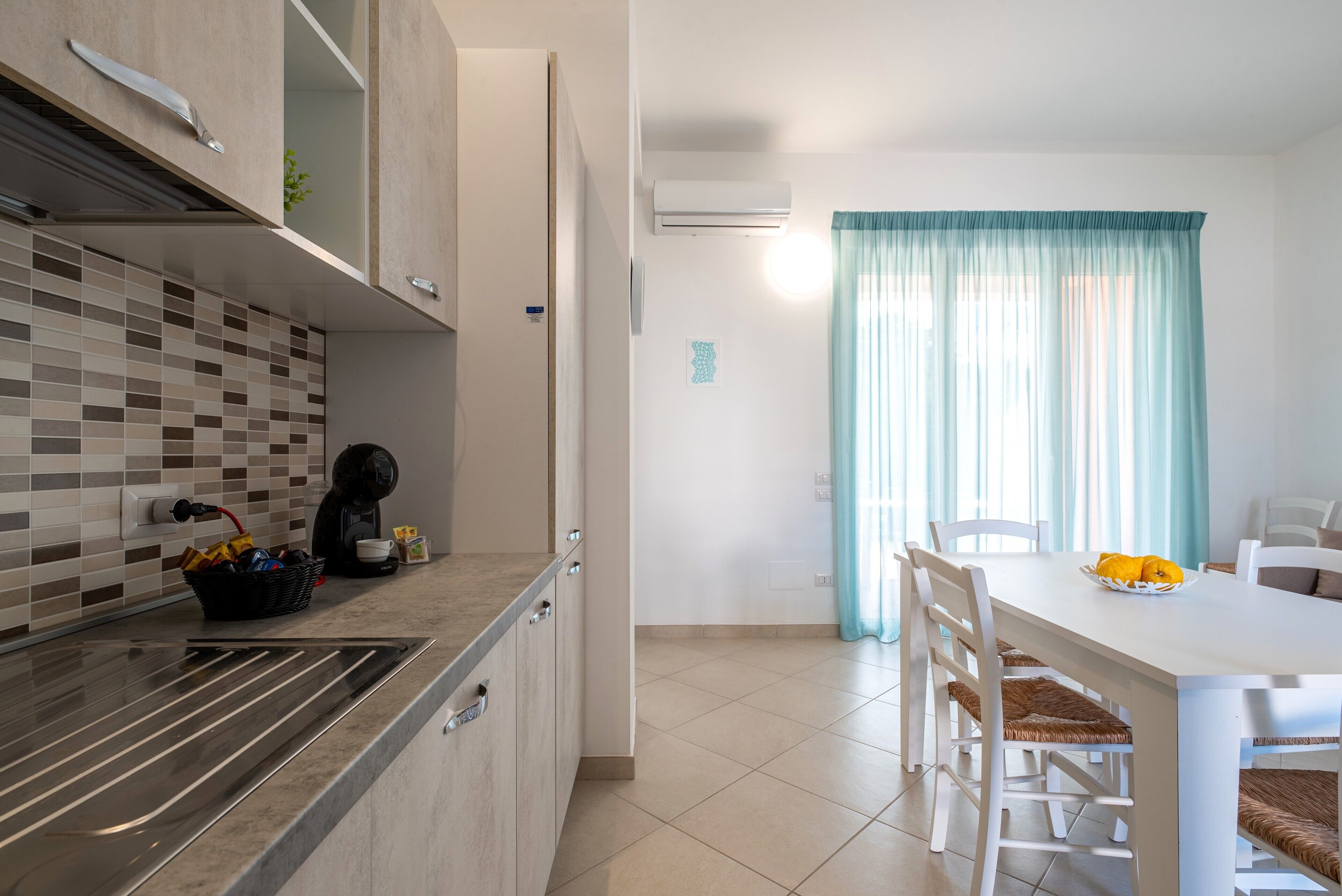 Una cuina moderna amb un mosaic protector, forn integrat i zona de menjador amb taula i cadires blanques.