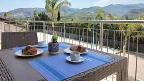 Un balcón con mobiliario de mimbre, una mesa con platos, tazas y una planta en maceta.