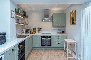 Una cocina compacta con armarios verde claro, horno empotrado y encimera blanca.