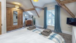 Un dormitorio con una cama grande, un armario de madera, un escritorio con silla, un televisor y una ventana con cortinas.
