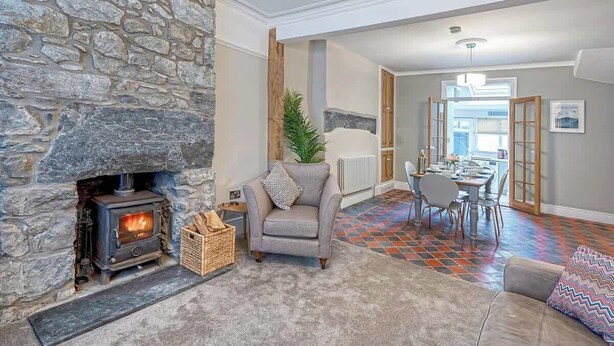 Una sala de estar acogedora con chimenea de piedra, un sillón cómodo y una zona de comedor con un estampado de suelo llamativo.