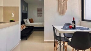 A compact living space with a kitchenette, a dining area with a table and chairs, a bed, and a macrame wall hanging.