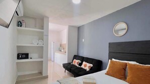 A bedroom with a bed, a black sofa, a white shelving unit, and a round mirror on the wall.