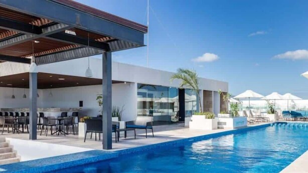 Un espace piscine moderne doté d’un coin salon couvert, de chaises longues et offrant une vue dégagée sur la piscine.