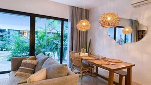 Un salon moderne comprenant un canapé, une table à manger et des chaises, de grandes fenêtres donnant sur un paysage verdoyant, et deux lampes suspendues en osier.