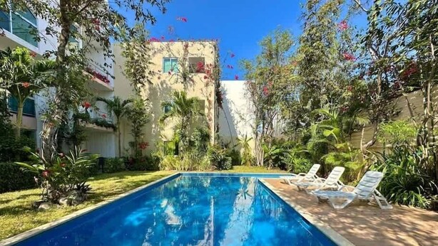 A swimming pool with lounge chairs, surrounded by lush greenery and a building in the background. - 3BR Apartment | 3 Ensuites | Pool | Near Beach (Playa del Carmen)