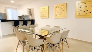 A modern dining area with a glass table surrounded by white chairs with wooden legs. There are three framed artworks on the wall above the table. - 3BR Apartment | 3 Ensuites | Pool | Near Beach (Playa del Carmen)