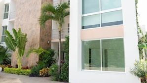 A modern building with large windows, a stone facade, and a landscaped garden with tropical plants. - 3BR Apartment | 3 Ensuites | Pool | Near Beach (Playa del Carmen)