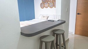 A small room with a bed, a desk, and two stools. - Downtown Cancún Garden Studio · WiFi & A/C (CancÃºn)