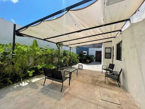 An outdoor patio with a shaded area, black metal furniture, and potted plants.