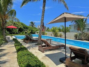 A poolside area with lounge chairs, a red umbrella, and a concrete pathway.