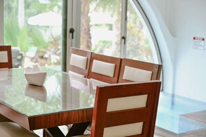 A dining table with chairs, a glass top, and a view of greenery outside.