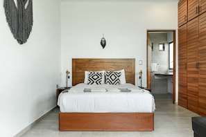 A bedroom with a wooden headboard, a bed with white bedding, two bedside lamps, and a wall-mounted dreamcatcher.