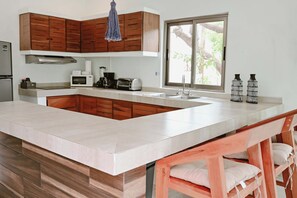 A modern kitchen with wooden cabinets, a large island, a built-in oven, and a window providing natural light.