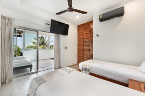 A hotel room with a balcony, a ceiling fan, an air conditioning unit, and two beds.