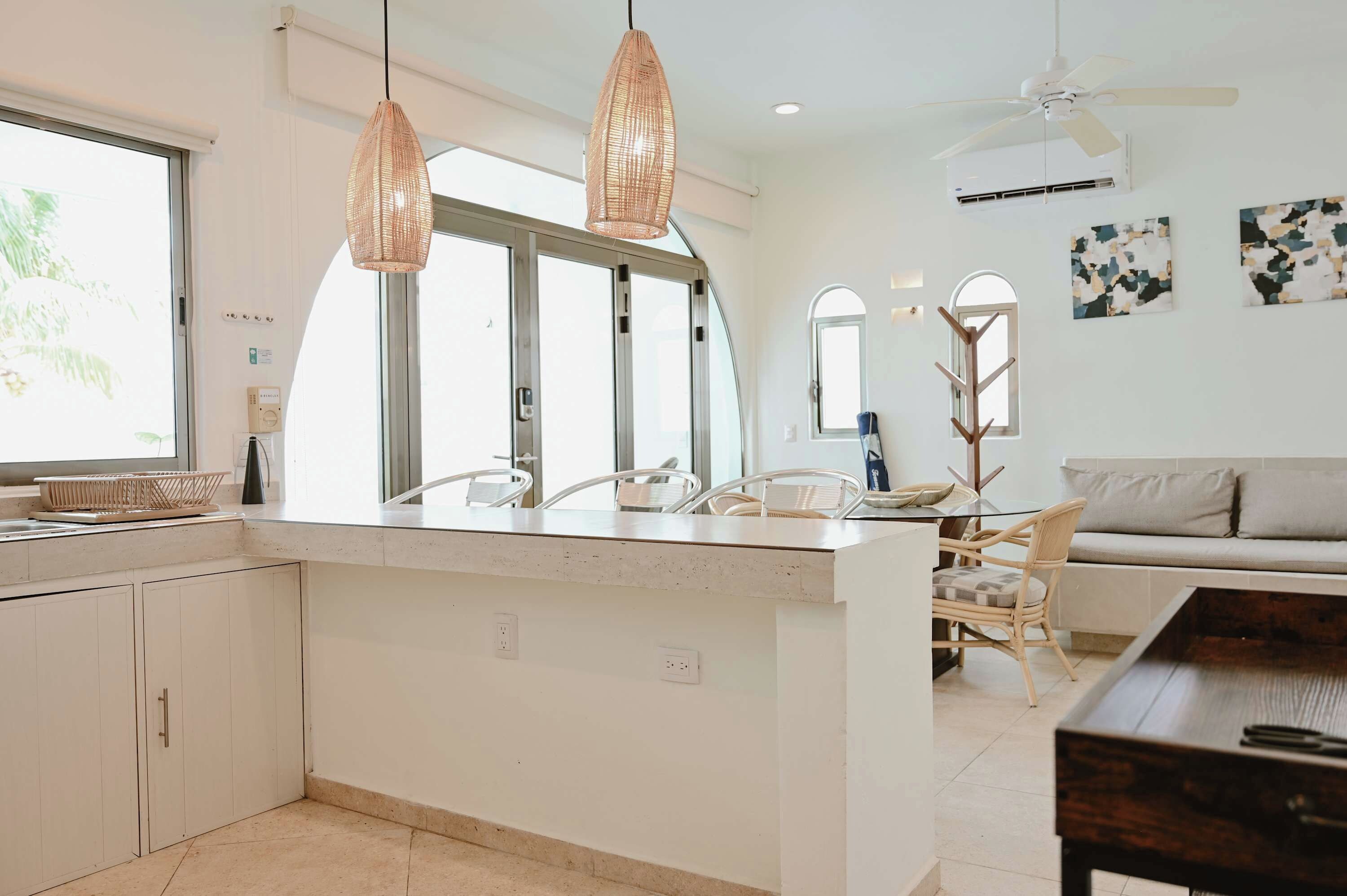 A modern kitchen with a central island, pendant lighting, and a dining area with a sofa and chairs.