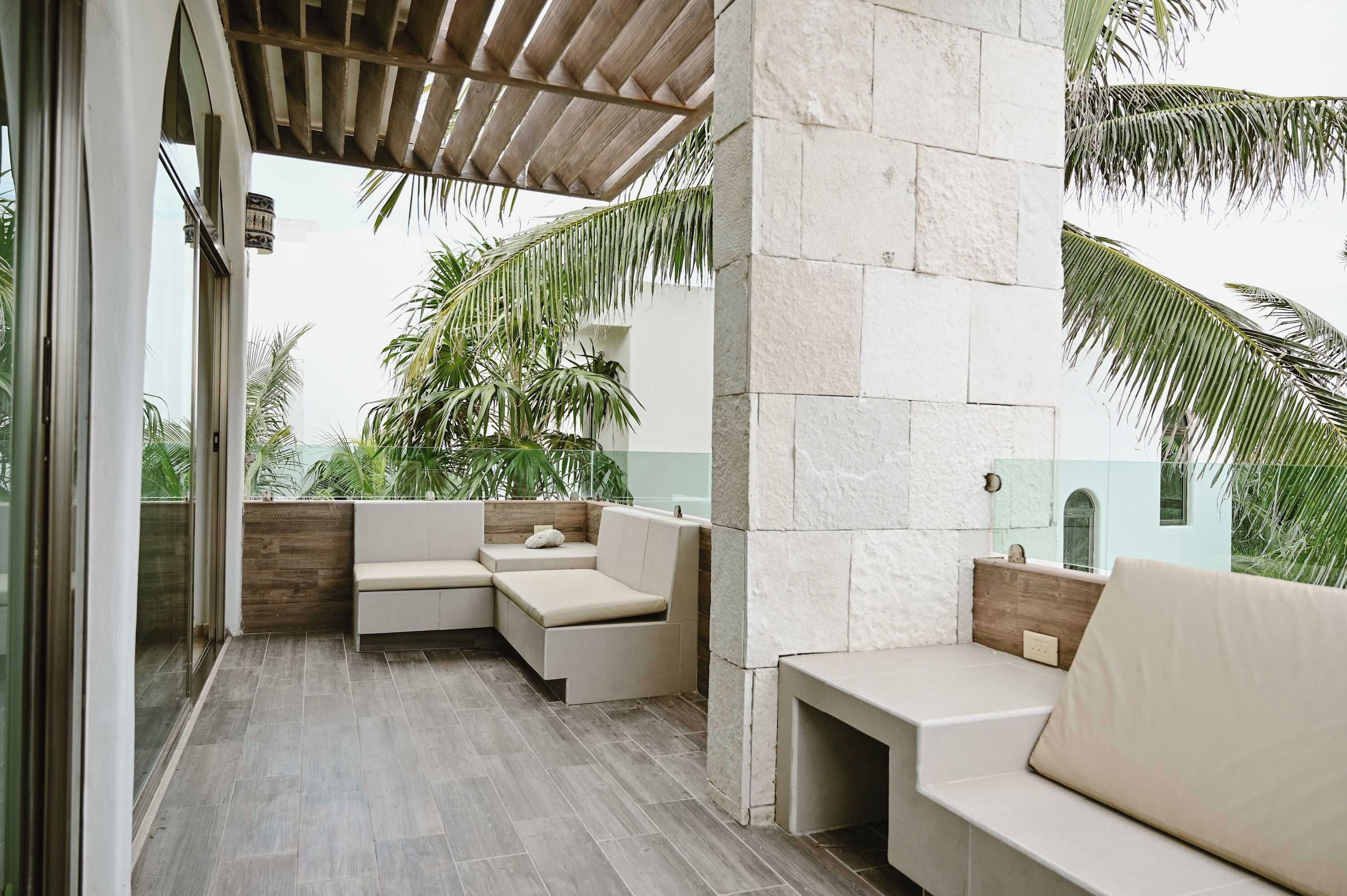 A modern outdoor seating area with a pergola, stone walls, and tropical plants.