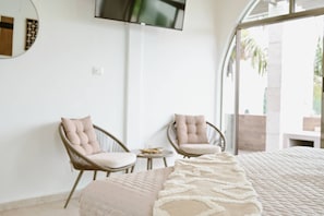 A bedroom with a bed, two chairs, a small table, and a TV on the wall.