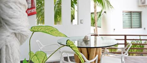 A room with a glass table, white chairs, a plant, and a fire extinguisher on the wall.
