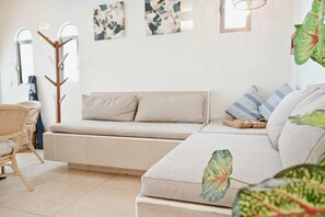 A modern living room with a sofa, a chair, and a coffee table. There are abstract paintings on the wall and a window providing natural light.