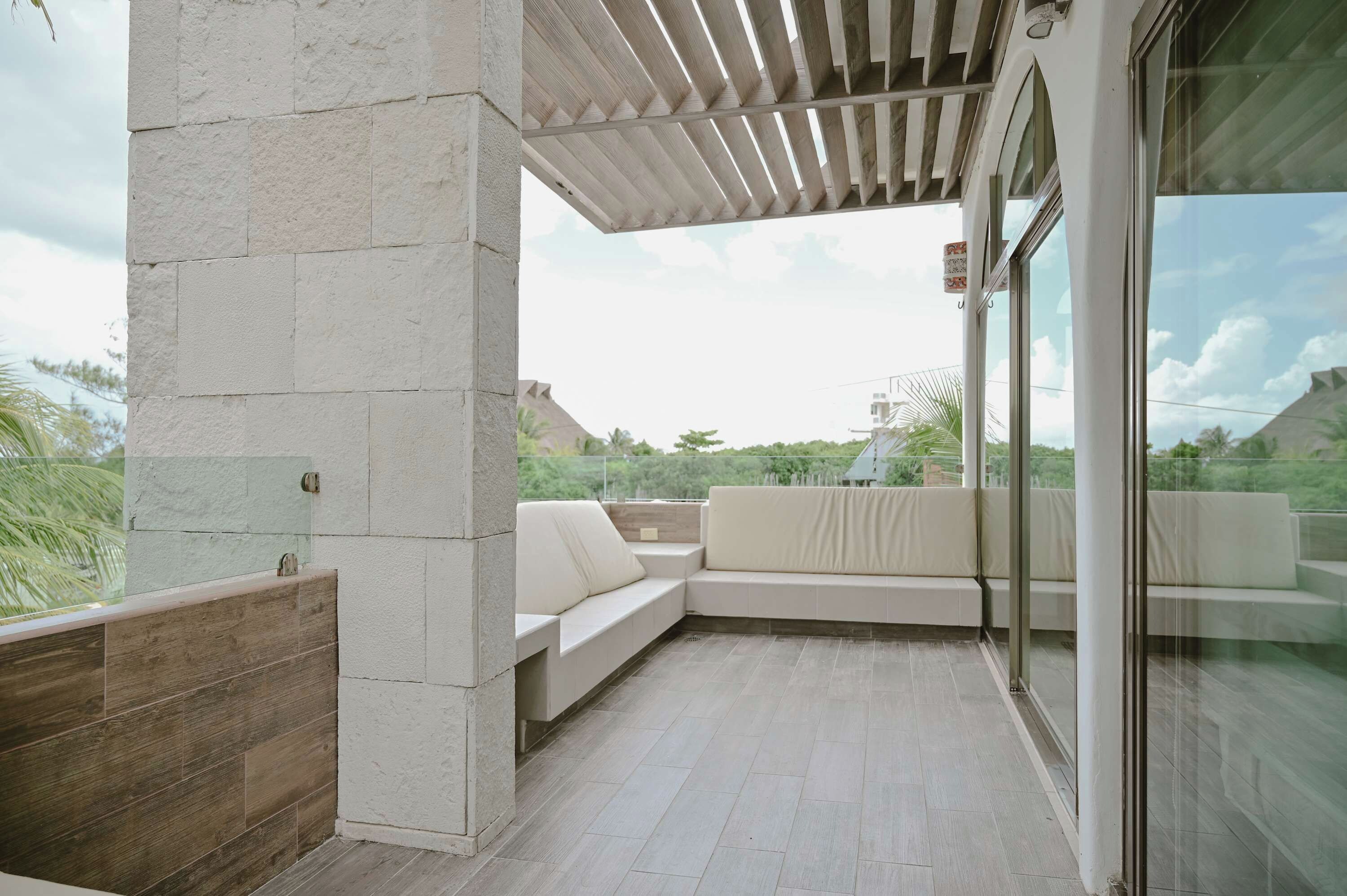 A modern outdoor seating area with a glass partition, a wooden pergola, and a view of the surrounding landscape.